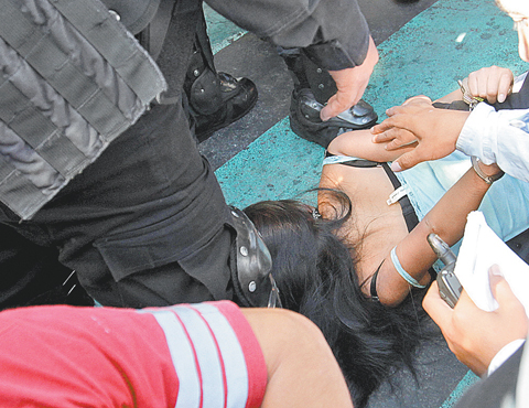 Policías detienen a una joven participante en los desmanes.
