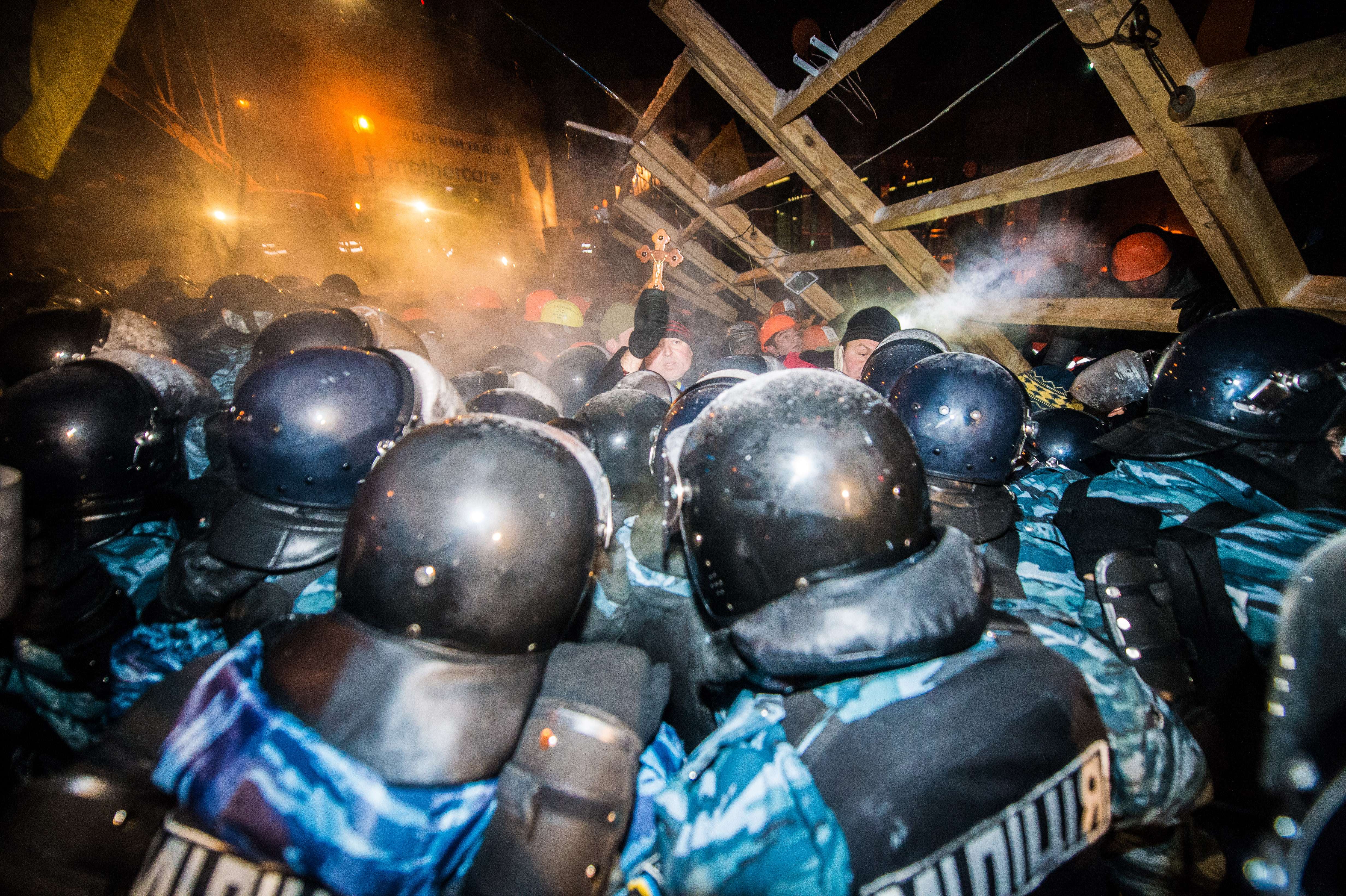 Un manifestante enseña una cruz al enfrentarse a policías antidisturbios que asaltan una barricada en la plaza de la Independencia de Kiev 