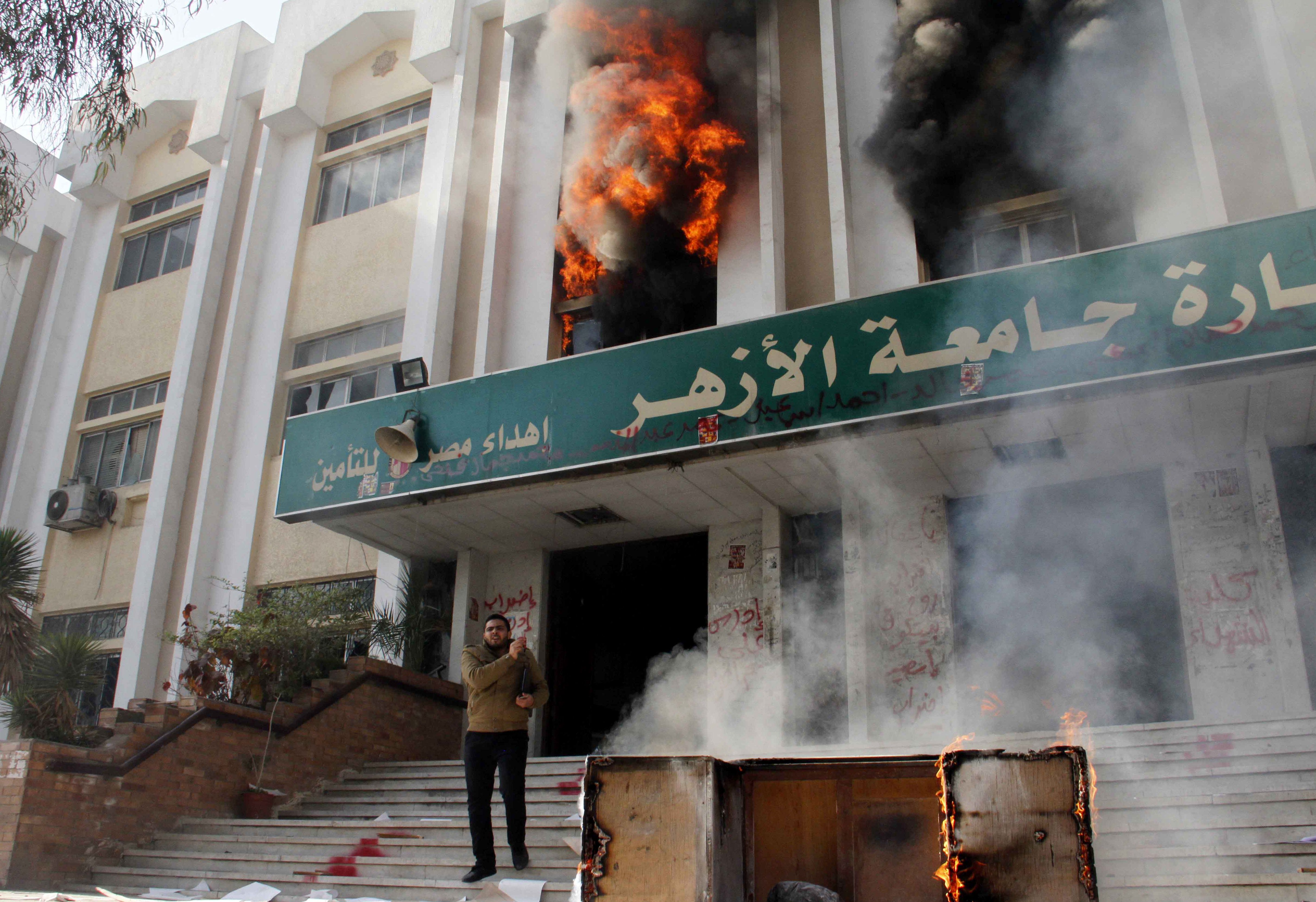 Un hombre permanece de pie ante un edificio de la universidad Al Azhar, ardiendo tras ser incendiado por estudiantes islamistas