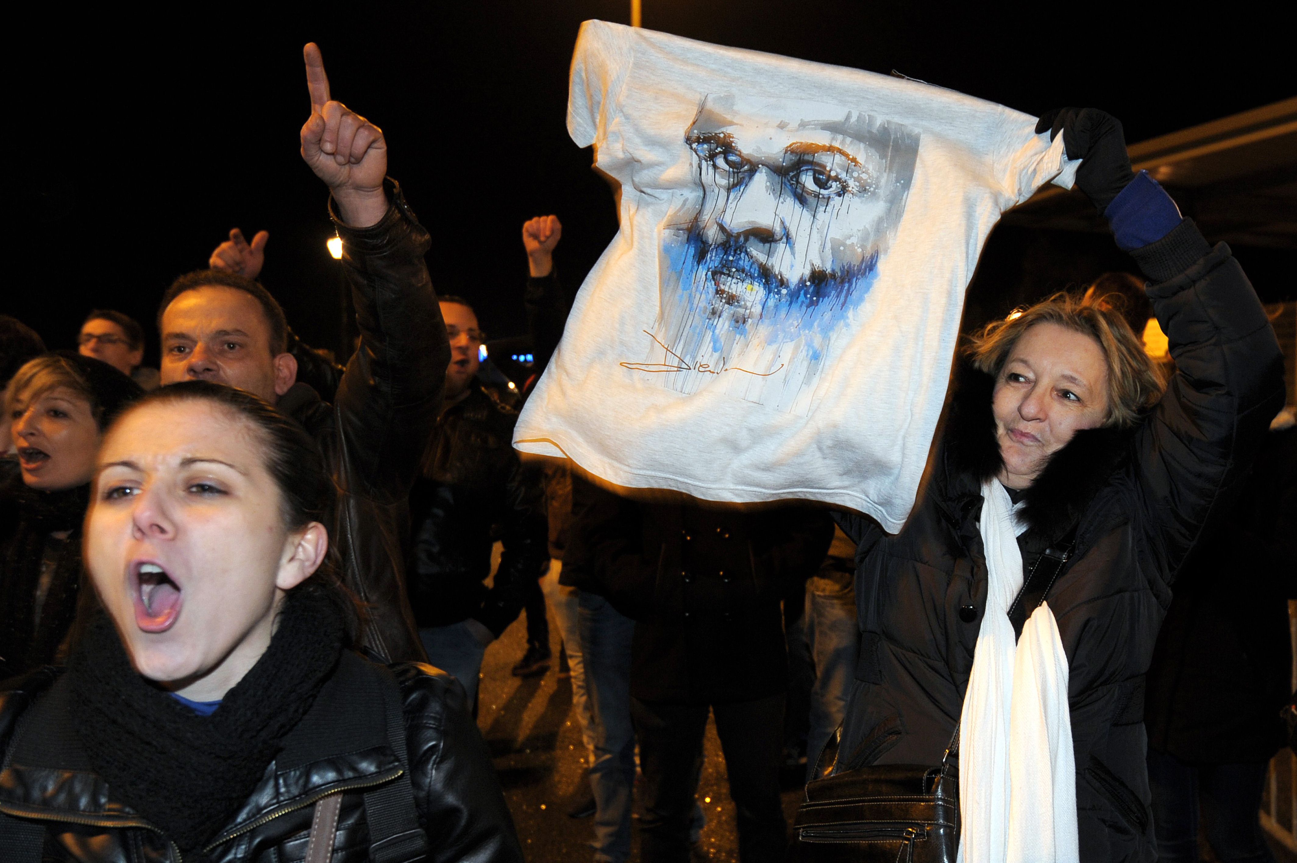 Una mujer (d) sostiene una camiseta con un dibujo del humorista Dieudonne M'bala M'bala tras conocerse que su actuación fue suspendida
