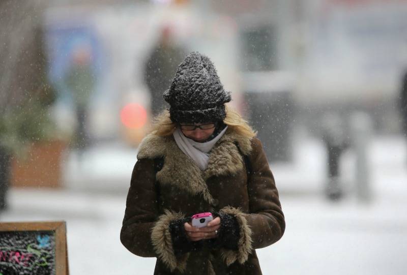 Una joven escribe en su celular mientras camina bajo la tormenta de nieve en NY.