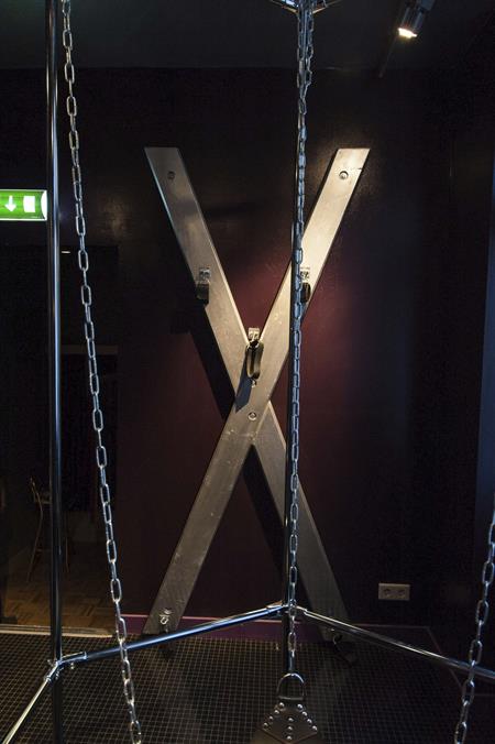Una de las salas dedicadas al sadomasoquismo con una cruz en forma de X sobre la pared y una "jaula" cerrada en cuyo interior el cliente permanece col