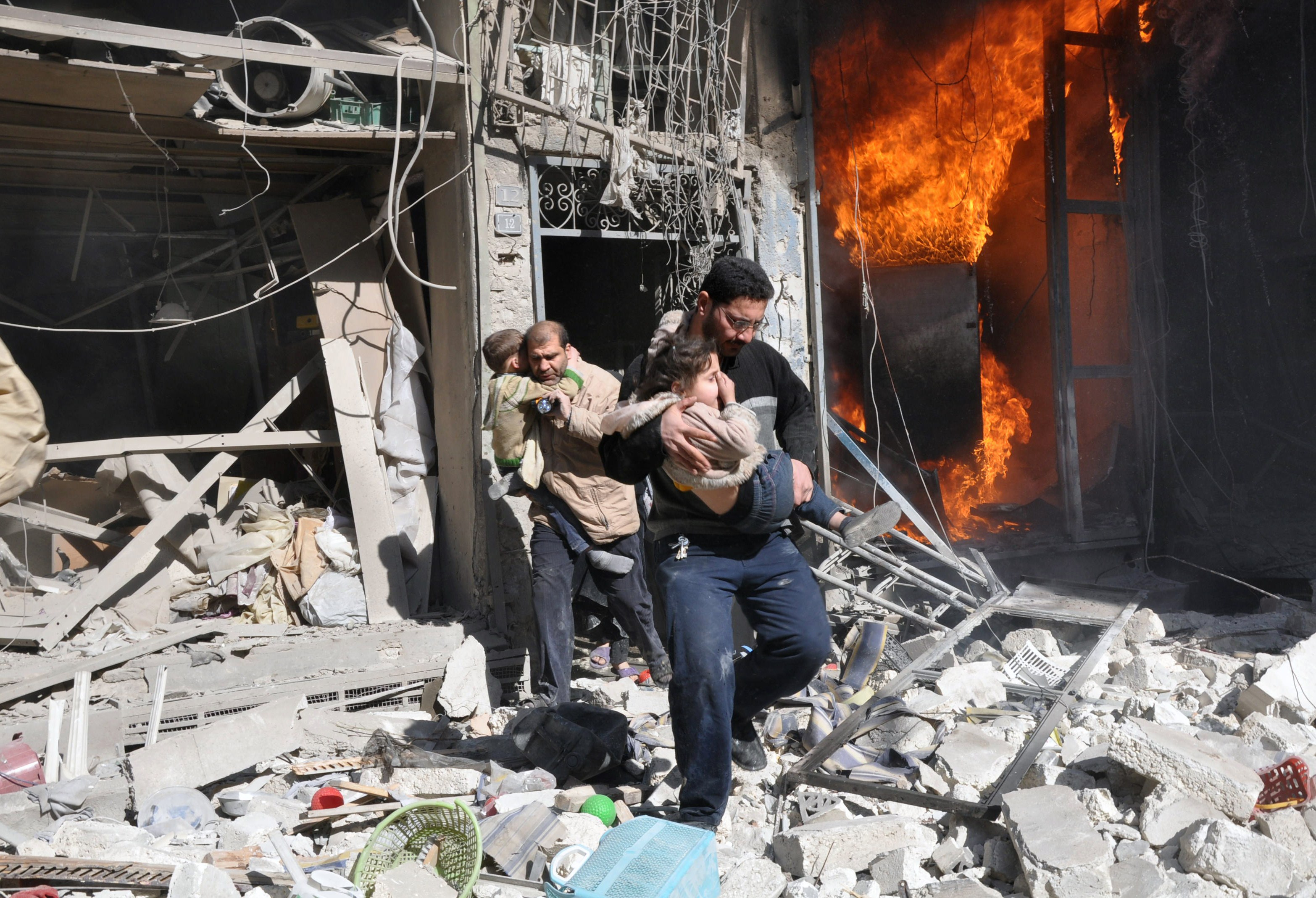 Dos hombres sacan a dos niños de un edificio en llamas tras el bombardeo de la aviación siria en Alepo