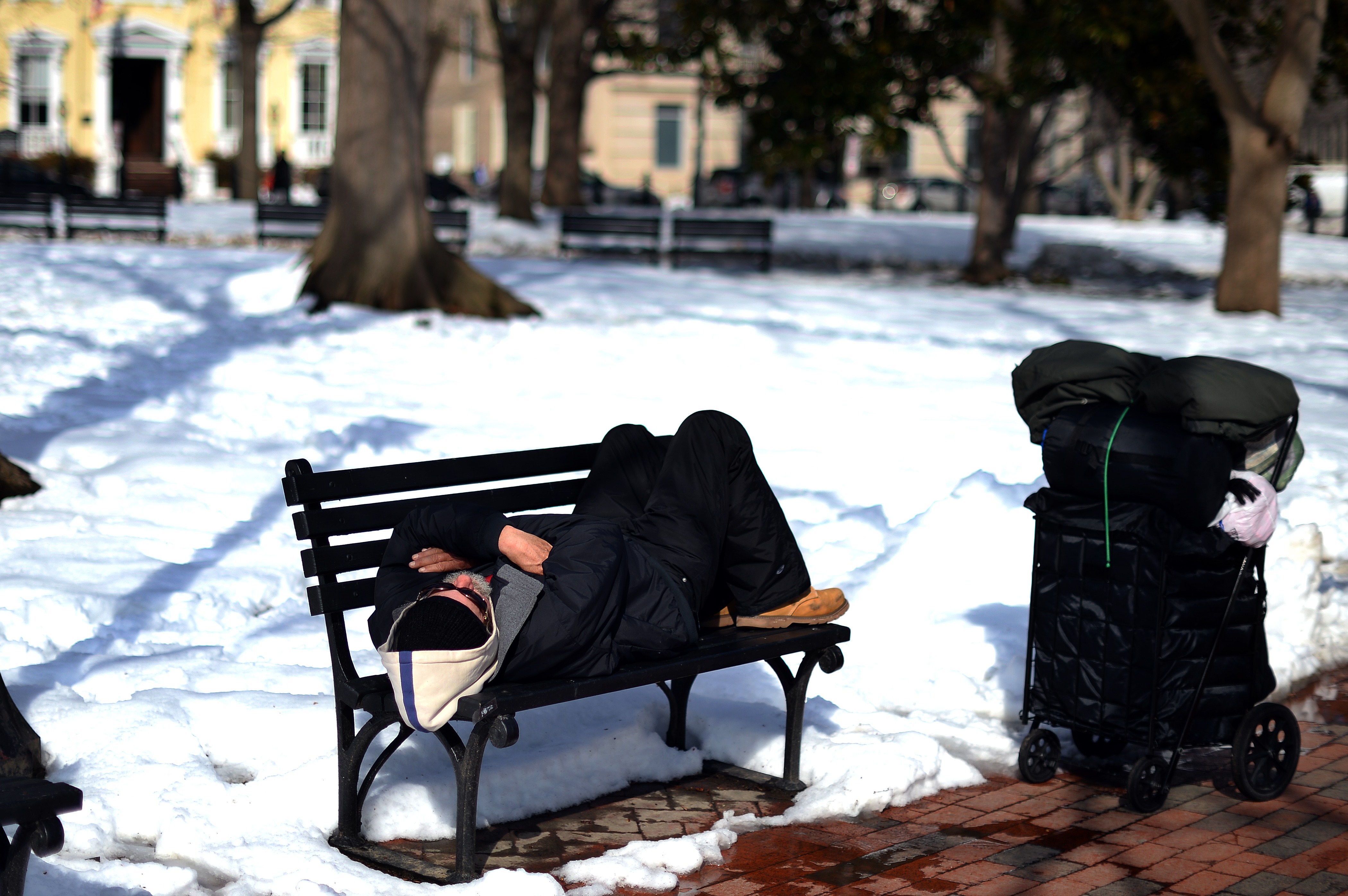 Un vagabundo descansa en un banco en el parque Lafayette, cubierto de nieve, cerca de la Casa Blanca