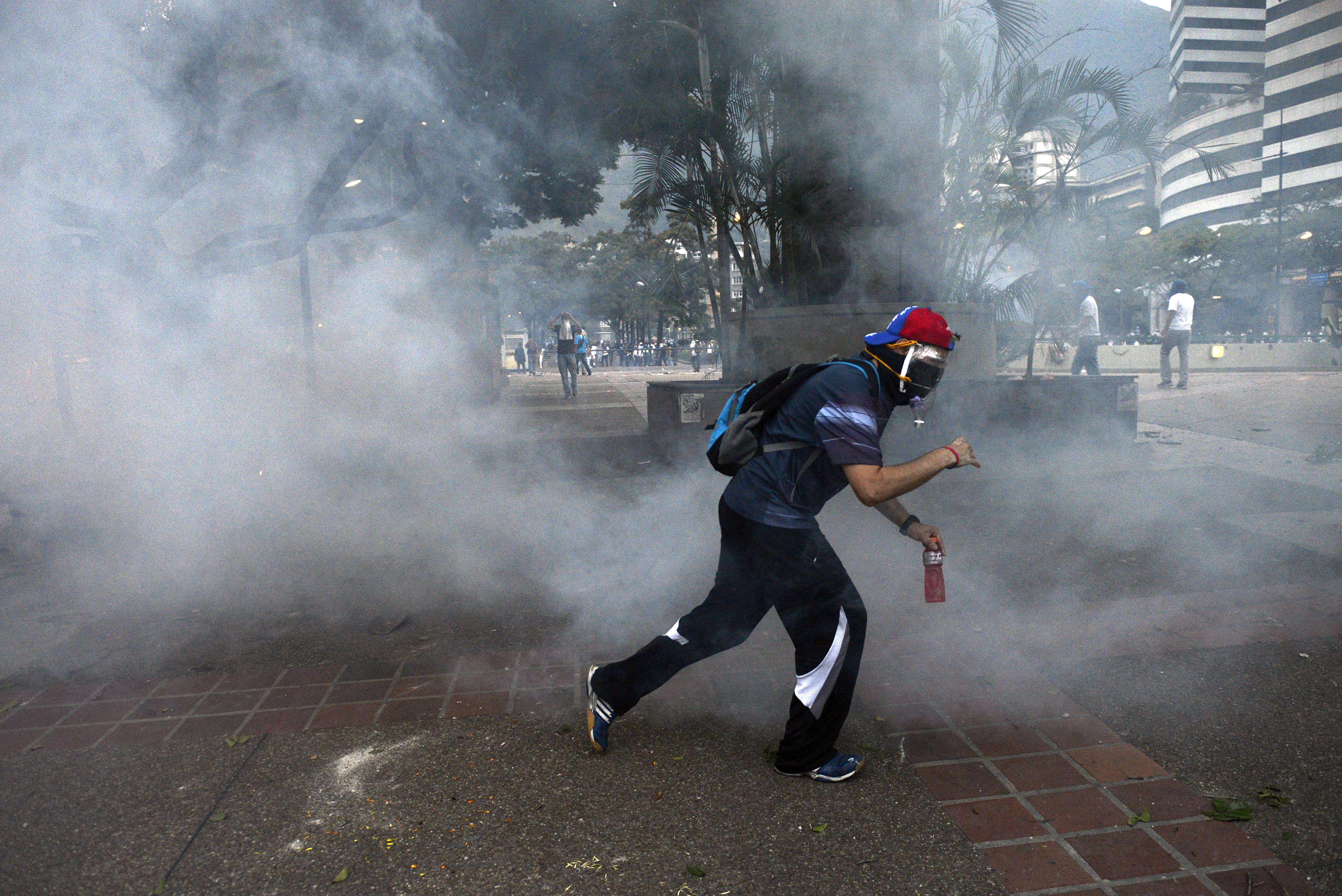 Manifestantes opositores intentan escapar de los gases lacrimógenos lanzados por la policía en Caracas
