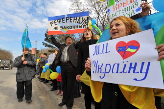 Un hombre (2i) sostiene un cartel que dice "Referéndum ilegal" y una mujer sostiene otro que dice "yo amo Ucrania" en una marcha tártara en Crimea