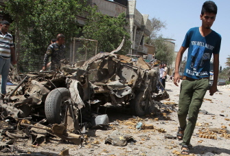 Un joven iraquí camina junto a los restos de un coche en el lugar de una explosión en Bagdad