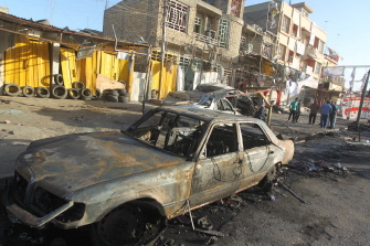 Iraquíes observan los restos de varios automóviles calcinados tras el estallido de un coche bomba en el barrio bagdadí de Ciudad Sadr