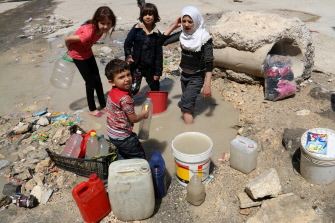 Niños sirios llenan cubos con agua turbia estancada al lado de una carretera en un sector de Alepo