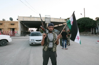 Un rebelde sostiene una bandera siria en el cruce de Bab al Salam, escenario del atentado de hoy, el 22 de julio de 2012