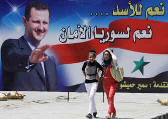 Jóvenes sirias caminan junto a un gran cartel de propaganda del presidente Asad con el lema "Sí a Asad... Sí a una Siria segura" 