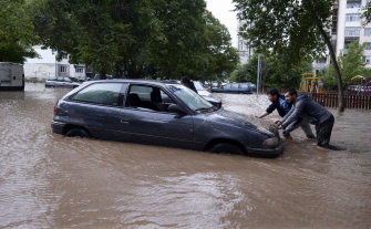 Dos personas intentan mover un automóvil en una calle inundada de Dobrich, en el noreste de Bulgaria