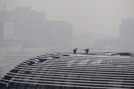Obreros en el tejado de un centro comercial en Pekín, con el cielo gris debido a la contaminación
