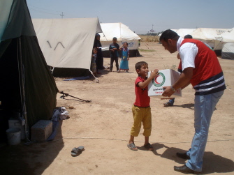 Un voluntario de la Media Luna Roja da un paquete de ayuda a un niño iraquí refugiado en un campo en Khanaqin, cerca de Irán