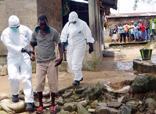 Dos enfermeros, vestidos con trajes especiales, escoltan a un enfermo de ébola en Monrovia, capital de Liberia