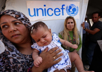 Una refugiada iraquí, que huyó de la violencia yihadista, sostiene un niño junto a una tienda de UNICEF en el campo de Bahrka, cerca de Erbil