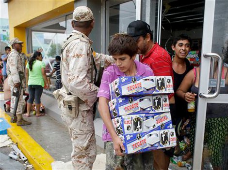 Un muchacho sale con cajas de cerveza de una tienda que permanecía abierta las 24 horas y que fue destruida por ‘Odila’ y el soldados intenta frenar a