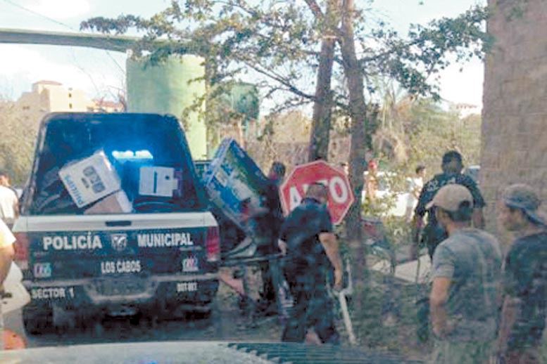 Policías municipales suben a una patrulla algunos productos en presuntos actos de rapiña.