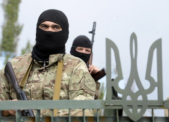 Miembros de la milicia proucraniana Santa María hacen guardia junto a una valla con el emblema nacional ucraniano en Mariupol