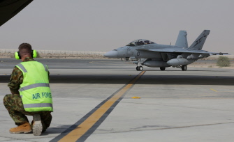 Un técnico australiano espera para guiar a un avión caza F/A-18F Super Hornet (d) australiano a su llegada  a una base en Oriente Medio