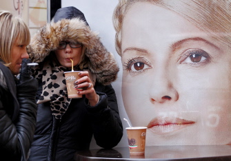 Una mujer fuma frente a un cartel electoral de Yulia Timoshenko mientras otra toma una bebida, en el centro de Kiev