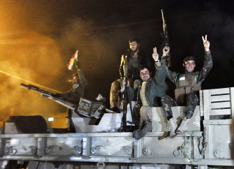 Combatientes kurdos peshmerga saludan en un vehículo militar con armamento de infantería mientras se dirigen a Kobane desde la turca Suruc