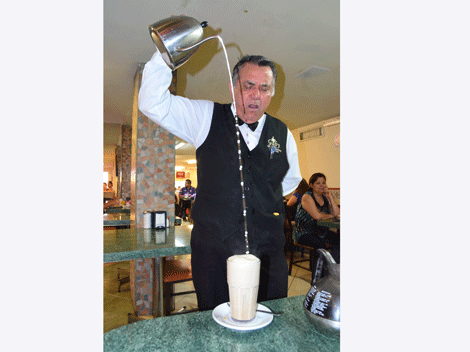 Al son de "Llegó el lechero", don Manuel Hernández, mesero de la cafetería Gaby, sirve la leche para los cafés.
