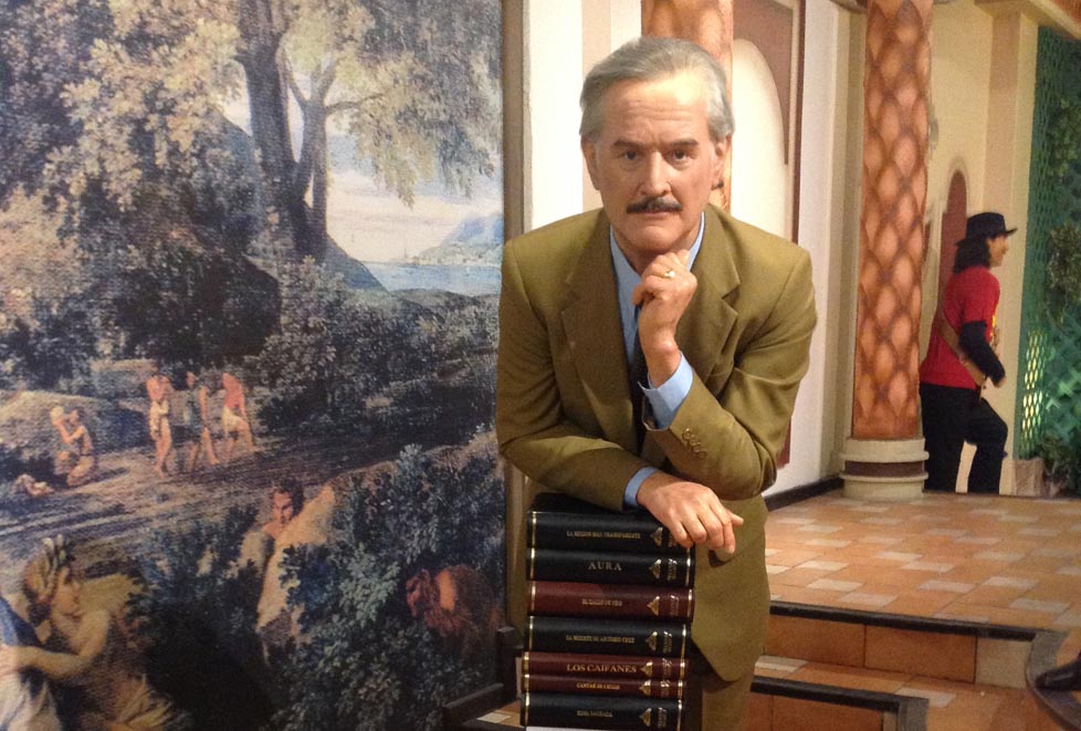 Carlos Fuentes aparece recargado sobre varios libros apilados de su autoría.