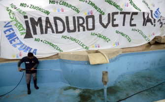 Un obrero limpia una fuente junto una pancarta con inscripciones contra el presidente venezolano Nicolás Maduro en Caracas