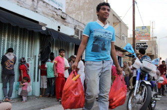 Un joven yemení lleva dos bolsas con pan mientras la gente espera afuera de una panadería en Taez 