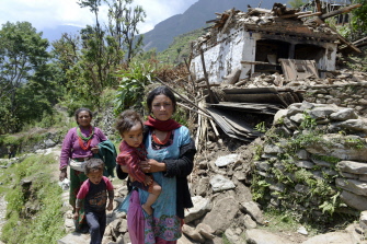 Dos mujeres nepalíes caminan con dos niños junto a un edificio destruido, camino de una consulta médica en Lapilang