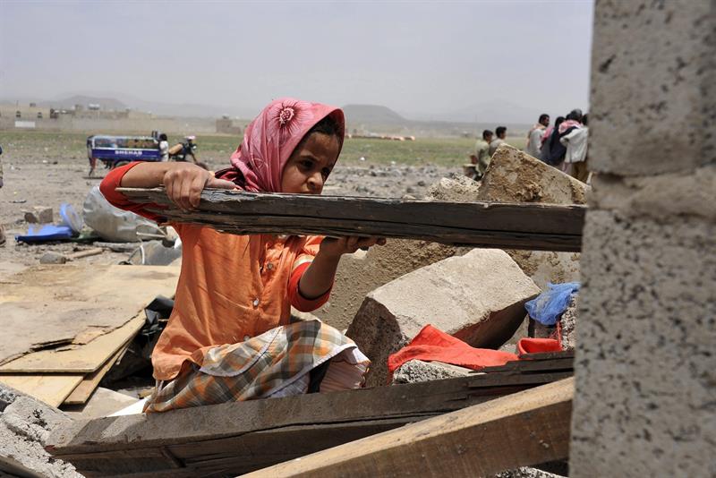 Una niña yemení recoge una viga de madera de su casa, destruída tras un bombardeo de la coalición liderada por Arabia Saudí, en Saná