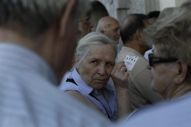 Una pensionista muestra su turno para entrar a cobrar parte de su sueldo a las afueras de una sucursal del Banco Nacional de Grecia en Atenas