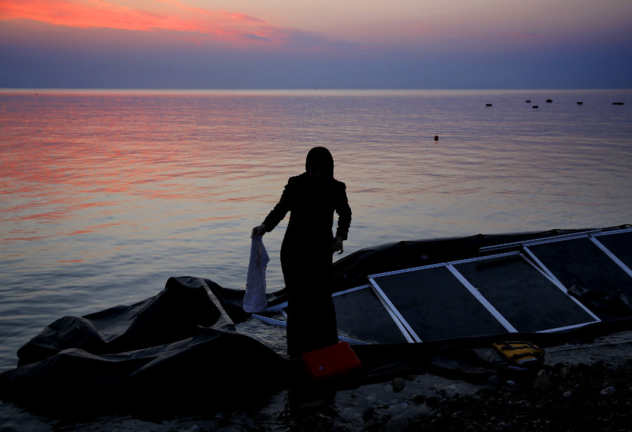Una mujer refugiada siria busca sus pertenencias alrededor de un bote desinflado en una playa en la isla griega de Kos, después cruzar, junto con dece