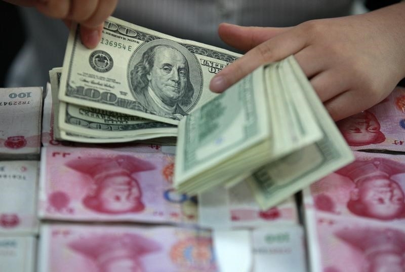 Un empleado del banco cuenta dólares estadounidenses sobre paquetes de billetes de 100 yuanes chinos.