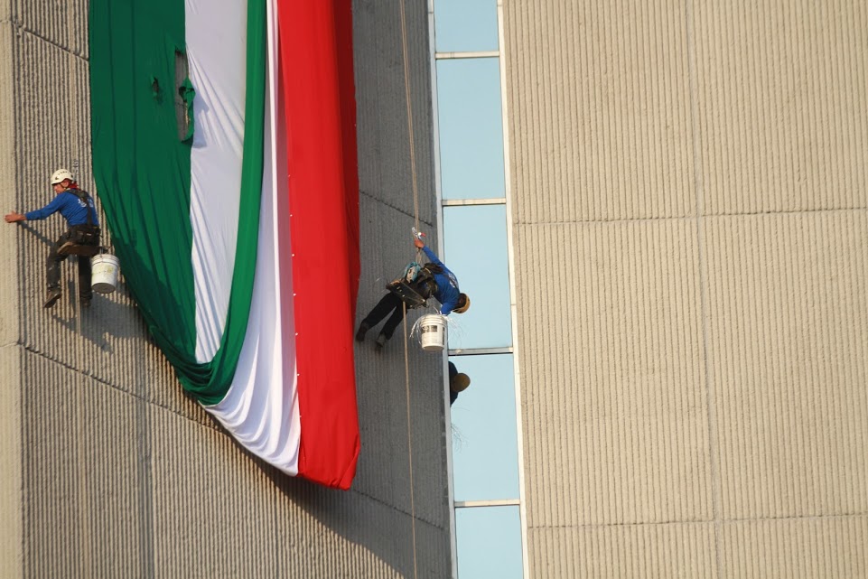 Trabajadores colocan los colores nacionales desde lo alto de un edificio.