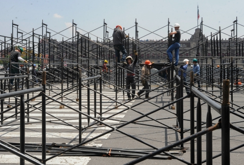 Personal del gobierno capitalino trabaja en el Zócalo en la instalación de adornos con motivos patrios.