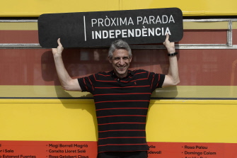 Un  hombre muestra un cartel con el lema "Próxima parada: independencia" junto a un autobús pintado con la bandera catalana, en Barcelona