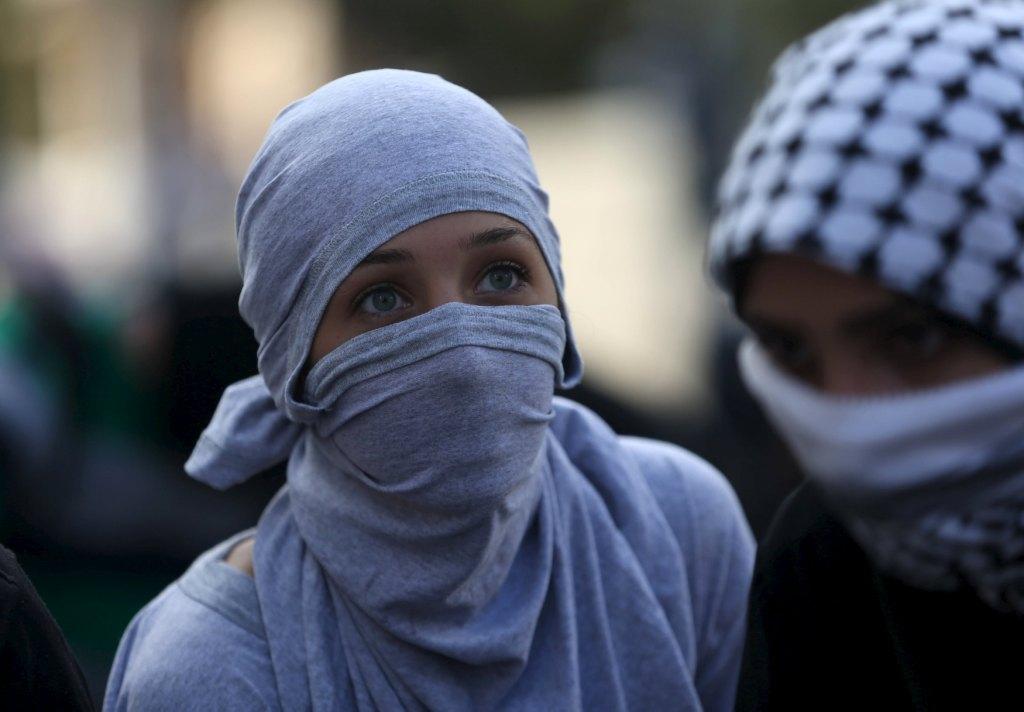 Con el rostro cubierto, jóvenes palestinas lanzan piedras y gritos a soldados israelíes. 