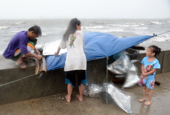 Una familia asegura su refugio temporal durante el fuerte viento y las lluvias traídas por el tifón Koppu en el bulevar Roxas, en Manila