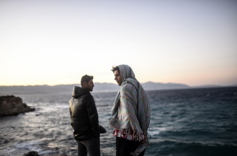 Dos migrantes miran hacia la isla de Chios mientras esperan que se calme el viento para viajar, en Cesme, en la provincia turca de Izmir