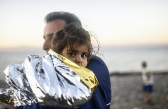Un hombre protege a una niña envuelta en una manta de emergencia, después de llegar con otros migrantes a la isla de Lesbos