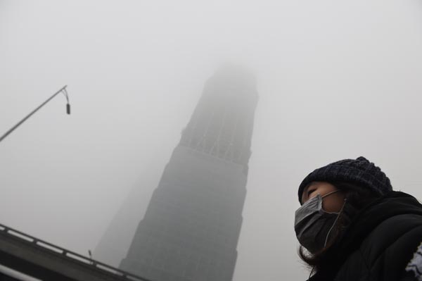 Una mujer espera a que un autobús debajo de un rascacielos envuelto en la niebla de humo en un día muy contaminada en Beijing el pasado 1 de diciembre