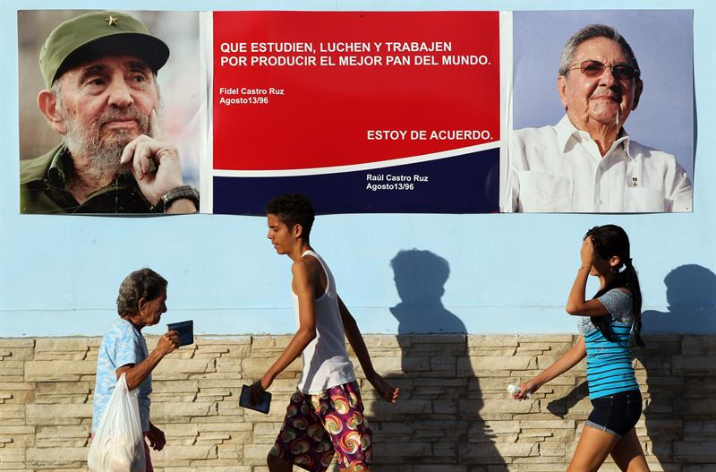 Varias personas caminan junto a un cartel con imágenes del líder cubano Fidel Castro y su hermano, el presidente Raúl Castro, en La Habana 