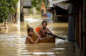 Niños filipinos usan un refrigerador como una barca para crucar una calle inundada en Candaba, Pampanga, al norte de la capital, Manila