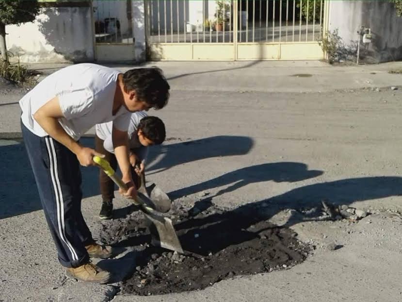 Adultos y niños participan en el 'bacheo' de las calles. 