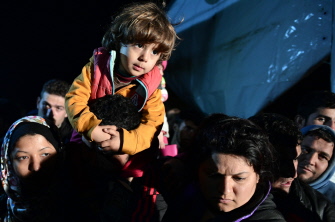 Refugiados cargan con sus niños mientras esperan a cruzar a Macedonia, en el puesto fronterizo de Idomeni, en Grecia