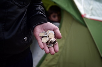 Un migrante muestra un puñado de euros mientras espera junto a otros refugiados por comida en el campo de Idomeni, Grecia
