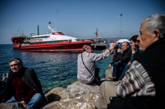 Un grupo de turcos observa desde unas rocas la llegada de un pequeño ferry con emigrantes deportados, en el puerto de Dikili, en Izmir, Turquía