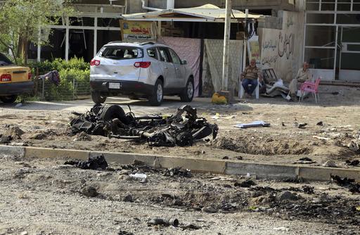 Varias personas permanecen sentadas cerca del lugar donde ocurrió un ataque suicida con coche bomba, en el barrio bagdadí de Hussainiyah